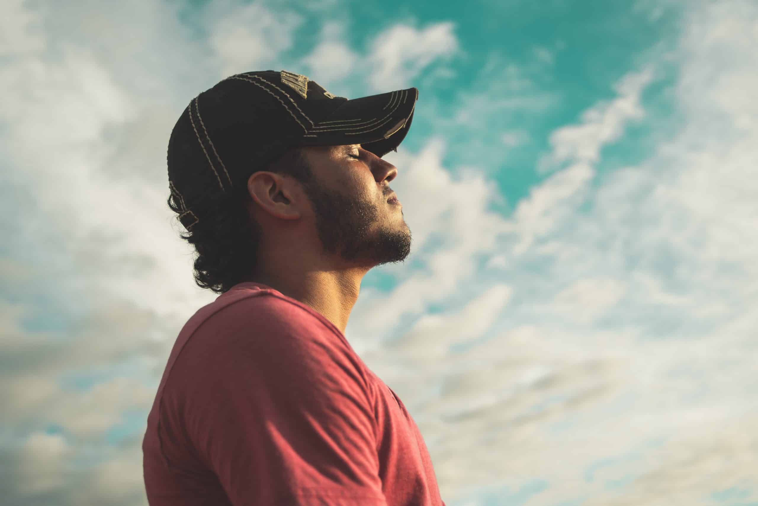 Man with cap in front of sky and breathing.
