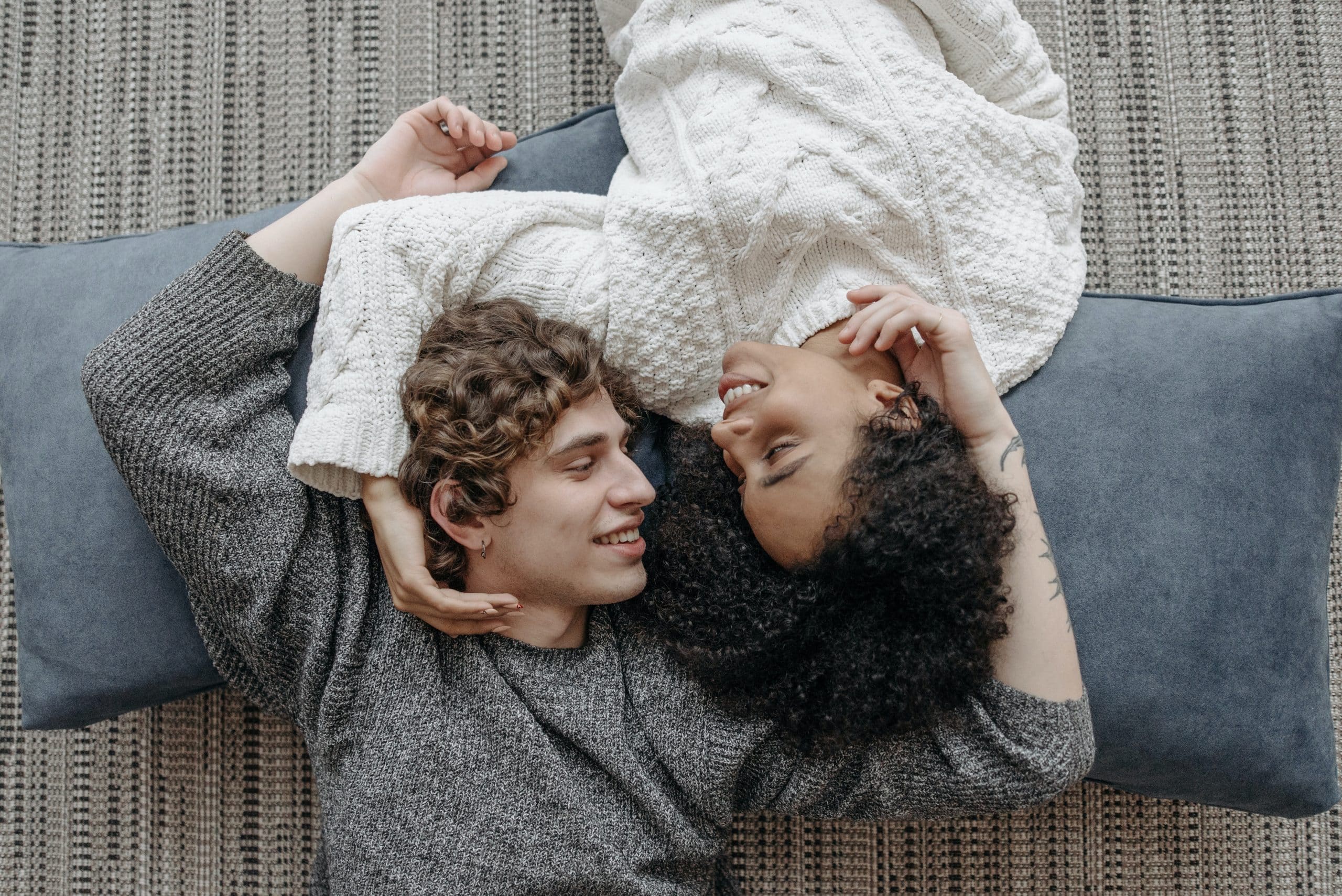 Vrouw en man liggen op de grond en kijken elkaar liefdevol aan.
